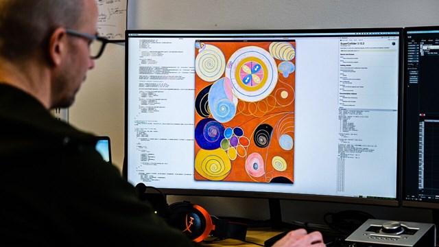 A person next to a computer with a painting by Hilma af Klint. 