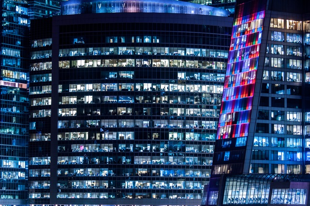Close up of skyscraper buildings lit up at night with neon colours.