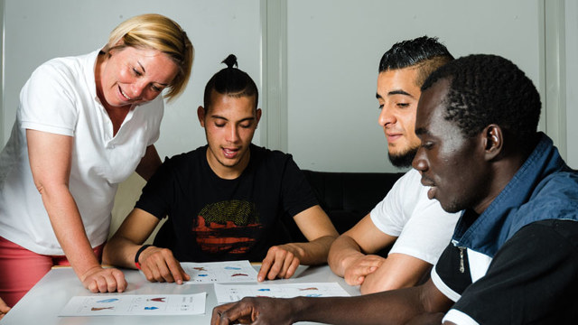 Language training for refugees in a German camp: A female German volunteer is teaching young refugees.