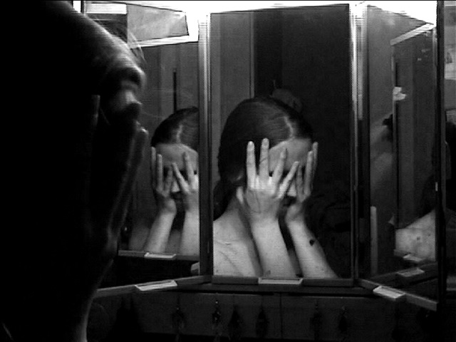 ung kvinna framför spegel döljer ansiktet i händerna