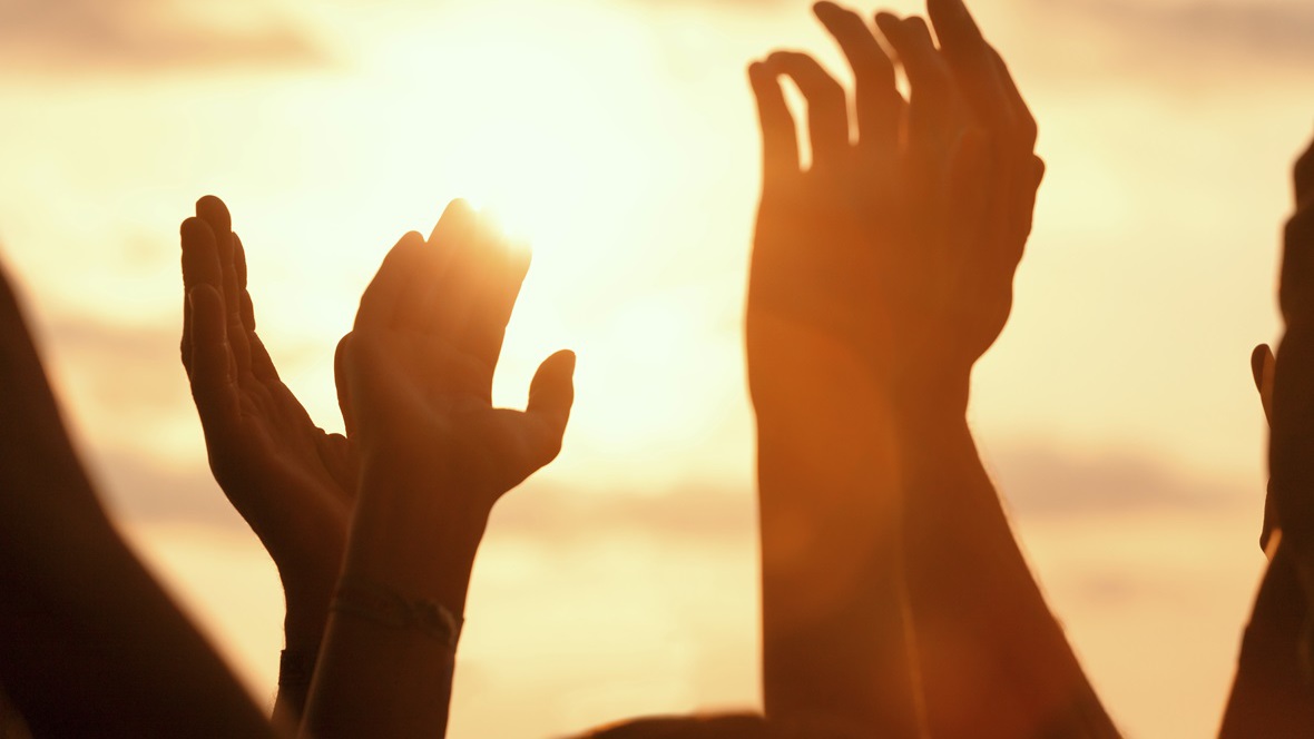Händer som sträcker sig upp i luften i solnedgång. 