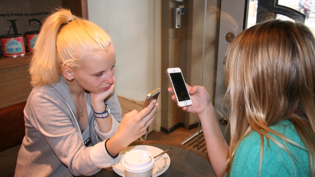 Två tjejer sitter på kafé med sina telefoner