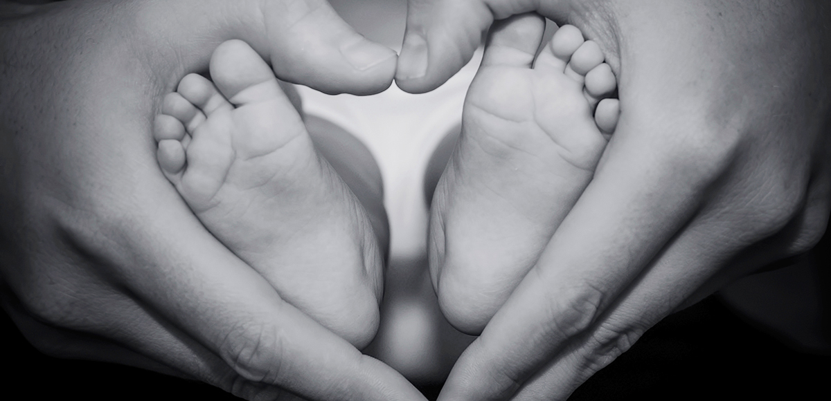 Händer bildar ett hjärta runt en babys fötter