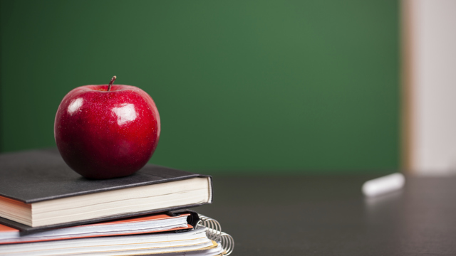 Äpple på böcker framför en grön tavla. Forskning om Didaktik och lärande.