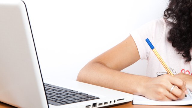 En ung tjej studerar. Använder dator, penna och anteckningsblock. / A young girl studying. She is using a computer, a pen and a notepad. 