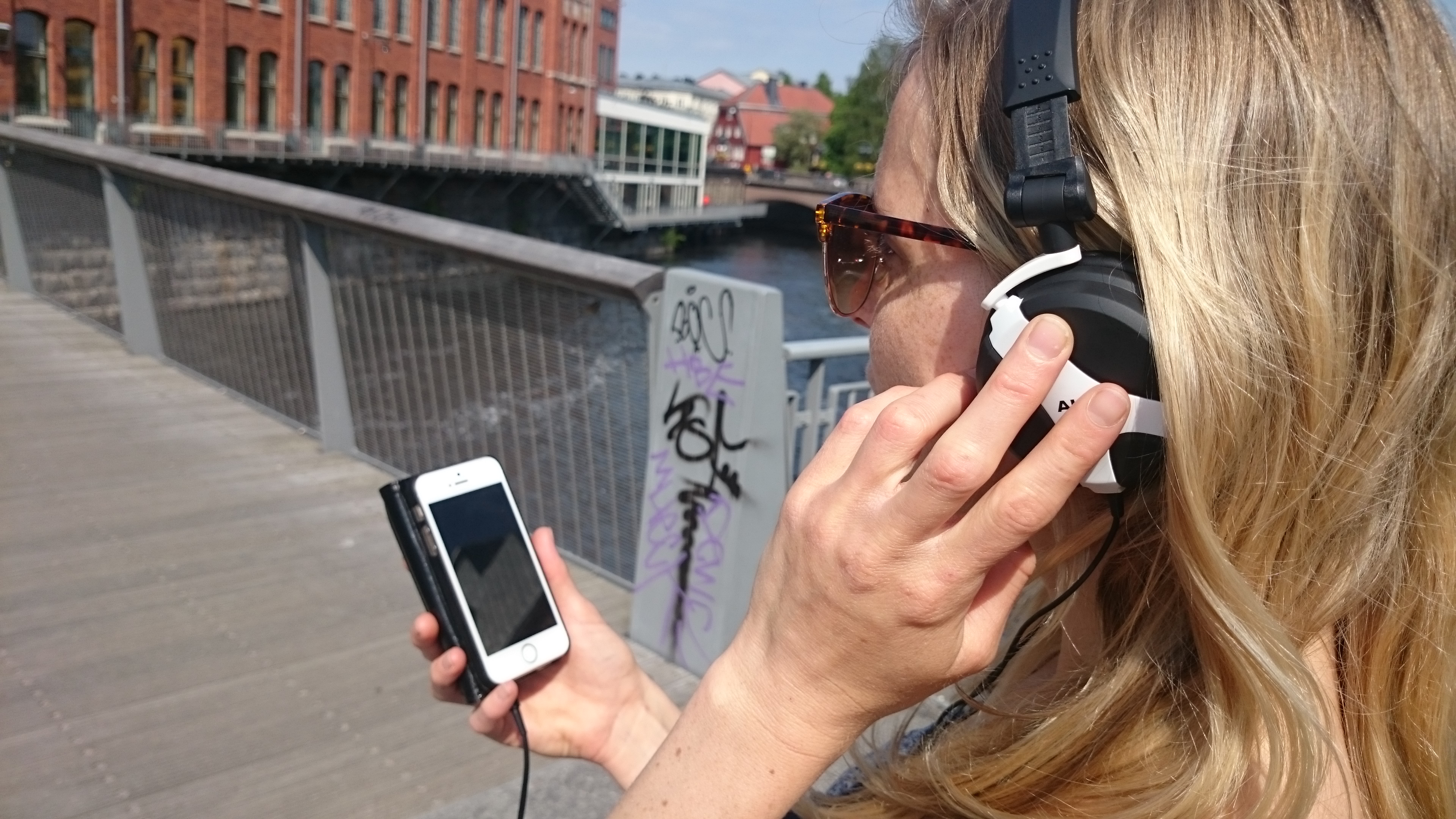 Kvinna med hörlurar och mobiltelefon utanför Kåkenhus vid Linköpings universitet i Norrköping.