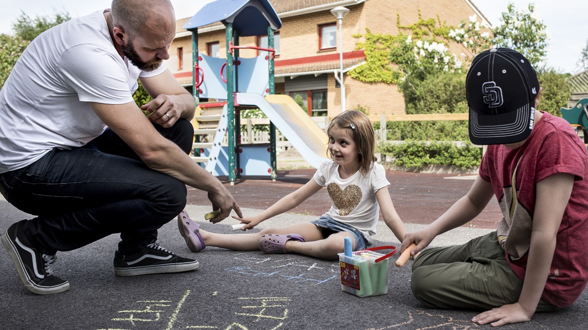 Fritidslärare ritar på asfalt tillsammans med två barn på en lekplats