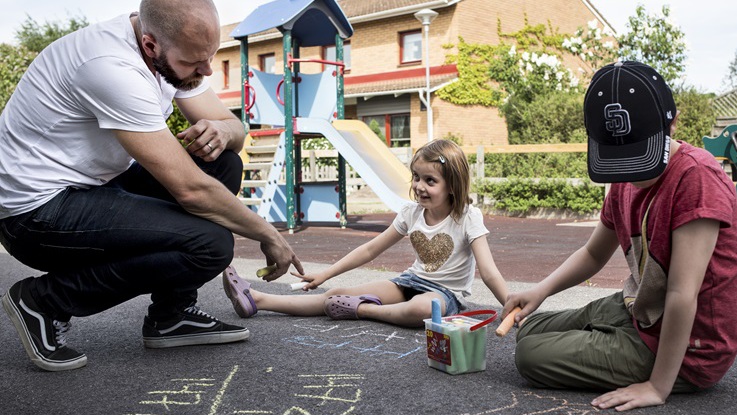 Fritidslärare ritar på asfalt tillsammans med två barn på en lekplats