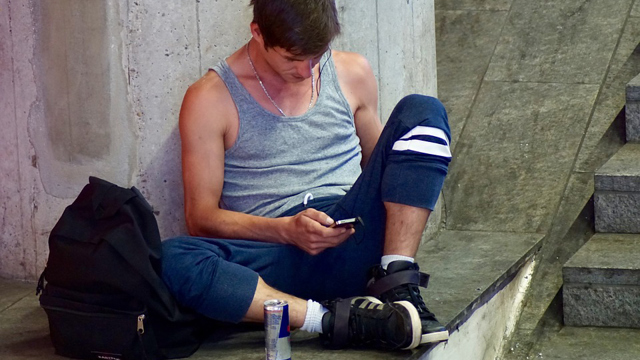 Ung man sitter utomhus med sin mobil