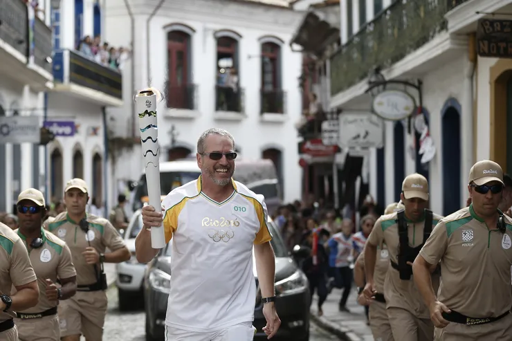 Man running with a torch. His t-shirt has the print Rio 2016. Men running around him with t-shirts with print Policia.