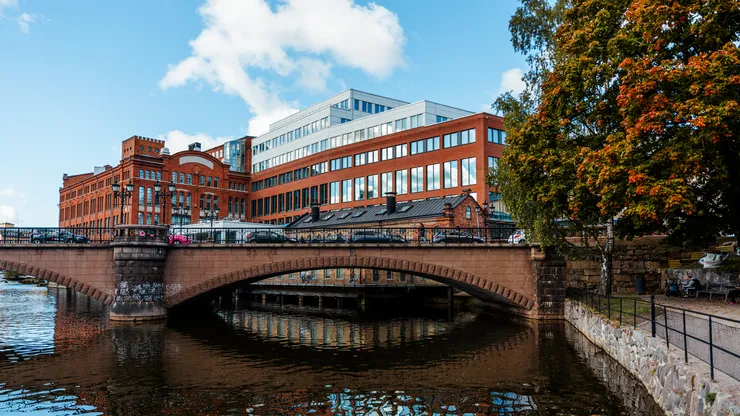 Water in front of a bridge and a building. Blue skies and a tree in autumn colours.