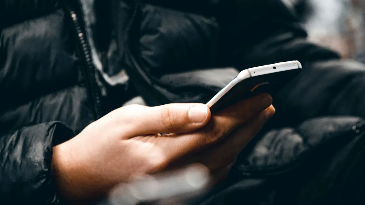 Person in black jacket sitting with a mobile phone in hand