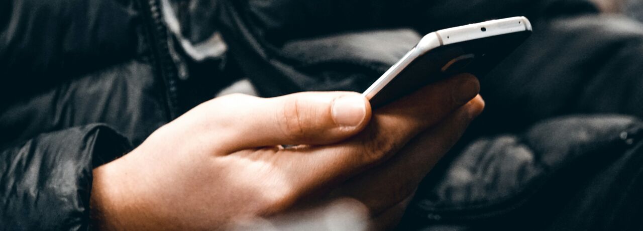 Person in black jacket sitting with a mobile phone in hand