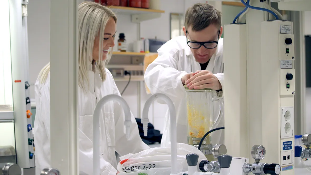 En man och kvinna i labbmiljö. Locket till en mixer hålls nere medan vätskor blandas.