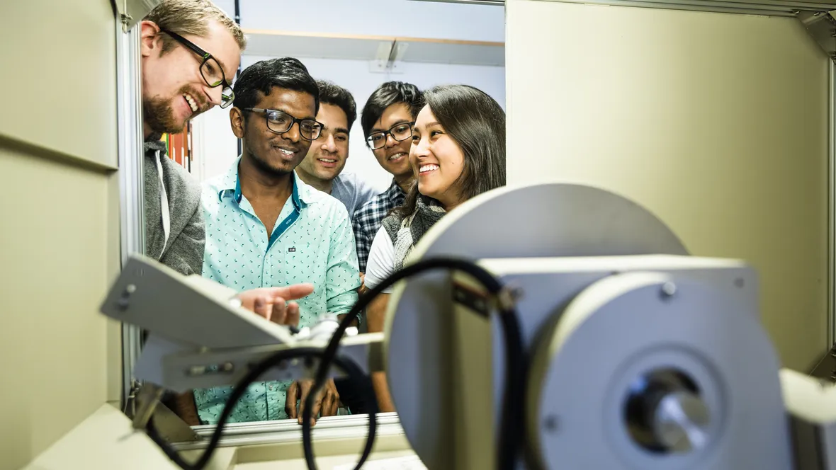 Glada studenter vid ingången till ett mindre rum med en teknisk apparat i.