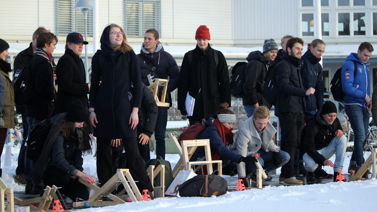 Studenter och mekaniska träapparater uppradade framför snötäcke