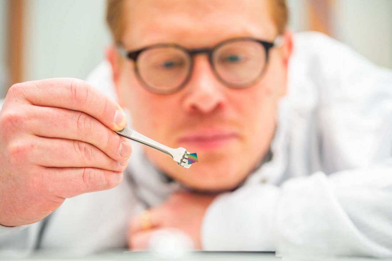 Person holding a small iridescent disc with tweezers.