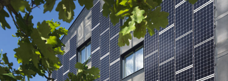 en husfasad med solcellspaneler och ett träd i förgrunden