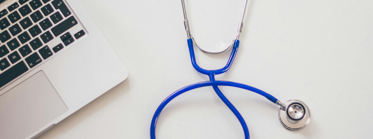 Blue stethoscope on a desk next to a laptop.