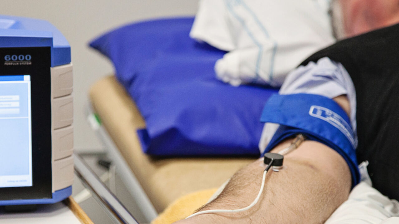 En person ligger på en sjukhussäng med en manschett runt armen som är kopplad till en enhet.