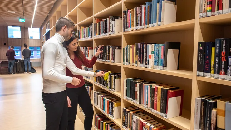 Two students at a books shelf in a library.