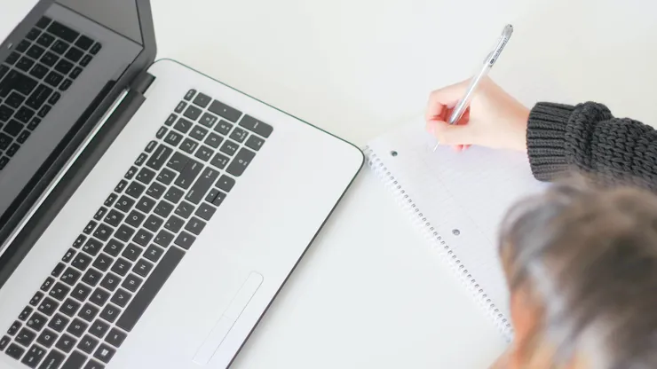 A photo of a computer, in the corner an arm taking notes is visible.