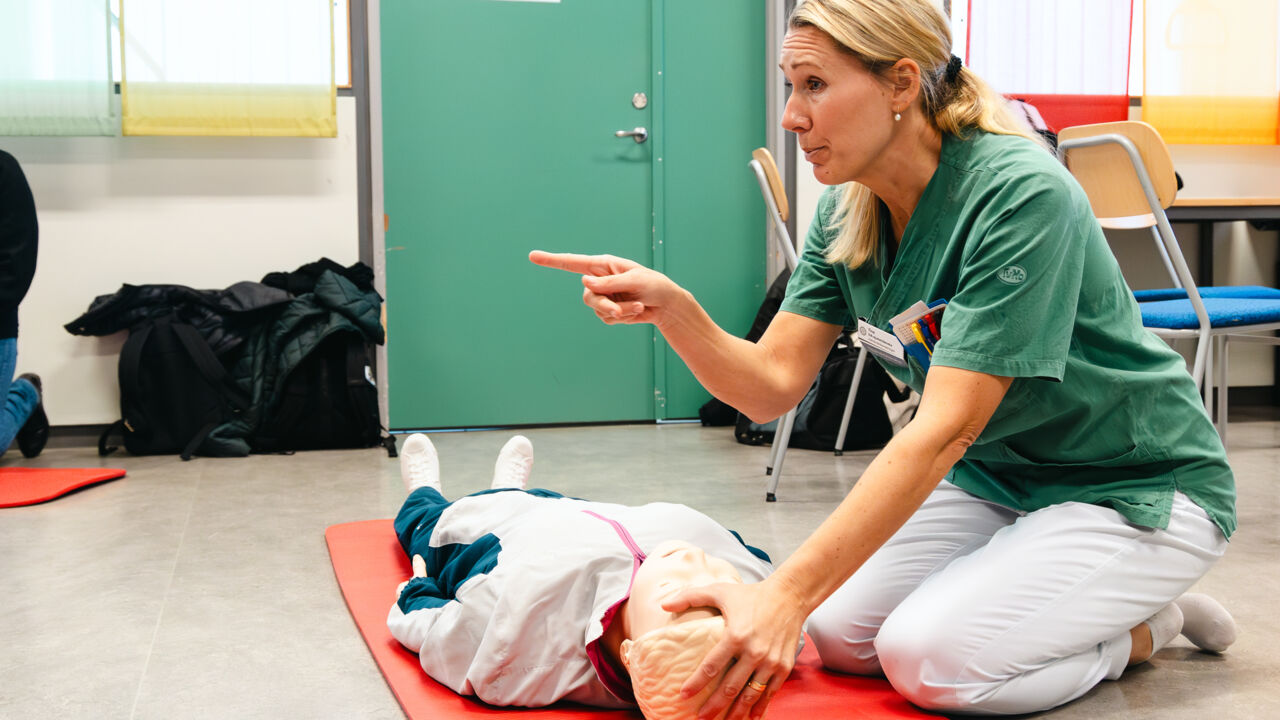 Woman in hospital clothes kneeling next to a manikin.