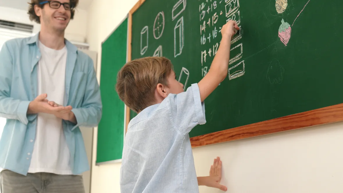 A pupil at the board counting a number. The teacher stands next to him and watches.