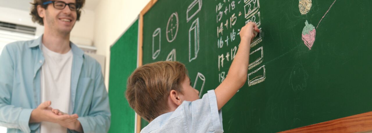 A pupil at the board counting a number. The teacher stands next to him and watches.