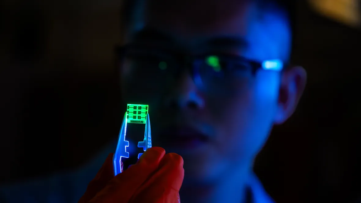 Researcher hold a glowing sheet of glass with tweezers.