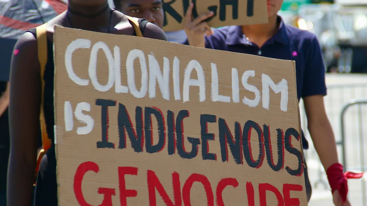 Demonstranter med plakat med texten COLONIALISM IS INDIGENOUS GENOCIDE
