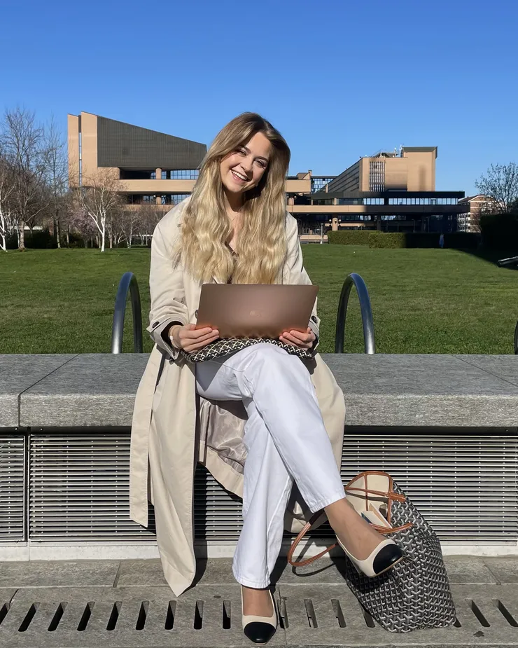 Kvinna sitter på bänk framför ett universitet