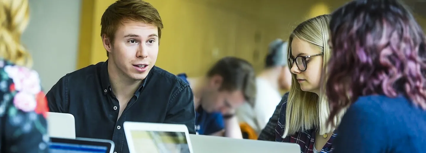 Tre studenter sitter och grupparbetar tillsammans. 