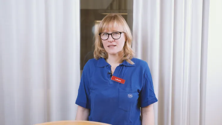 Person i blå läkarkläder står framöver vita gardiner.