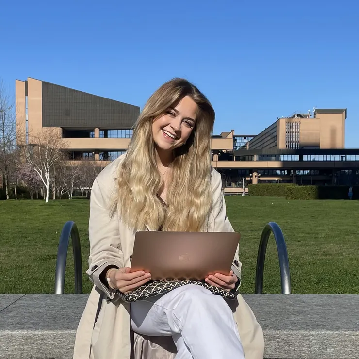 Kvinna sitter på bänk framför ett universitet