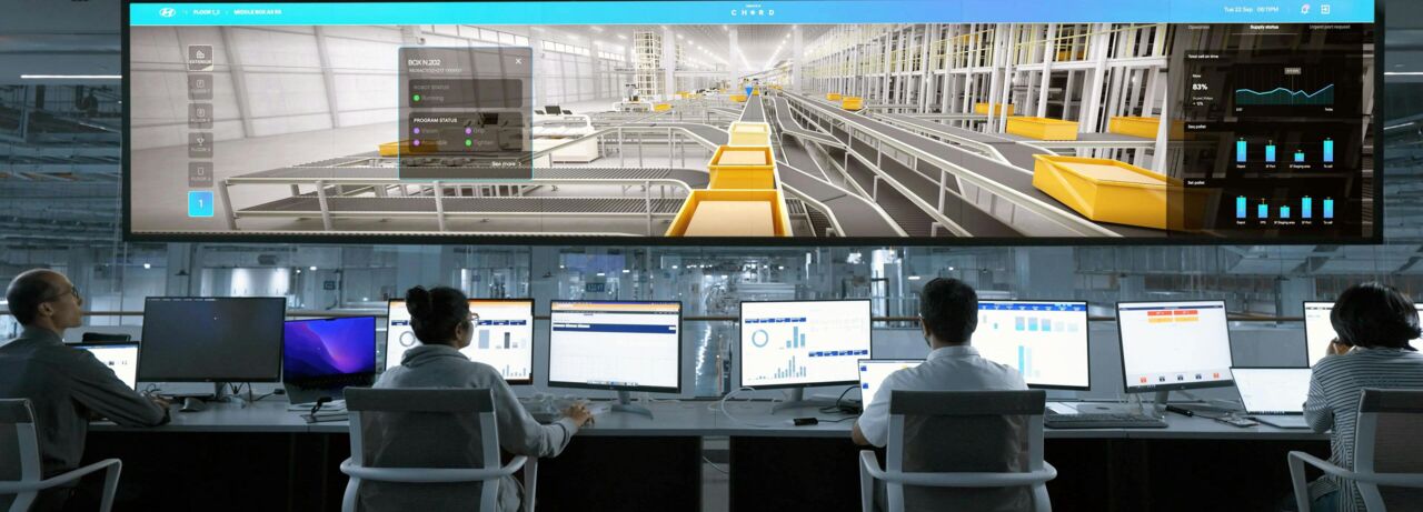 En grupp människor sitter vid skrivbord framför en stor skärm, engagerade i en presentation eller möte.