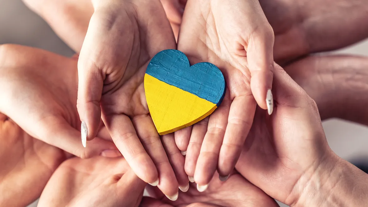 Händer som håller i ett hjärta i ett träd målat som Ukrainas flagga.