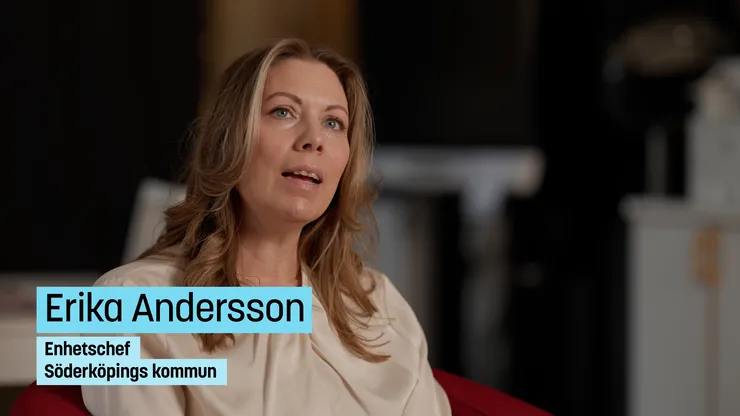 Långhårig kvinna i ljus blus sitter i fåtölj.