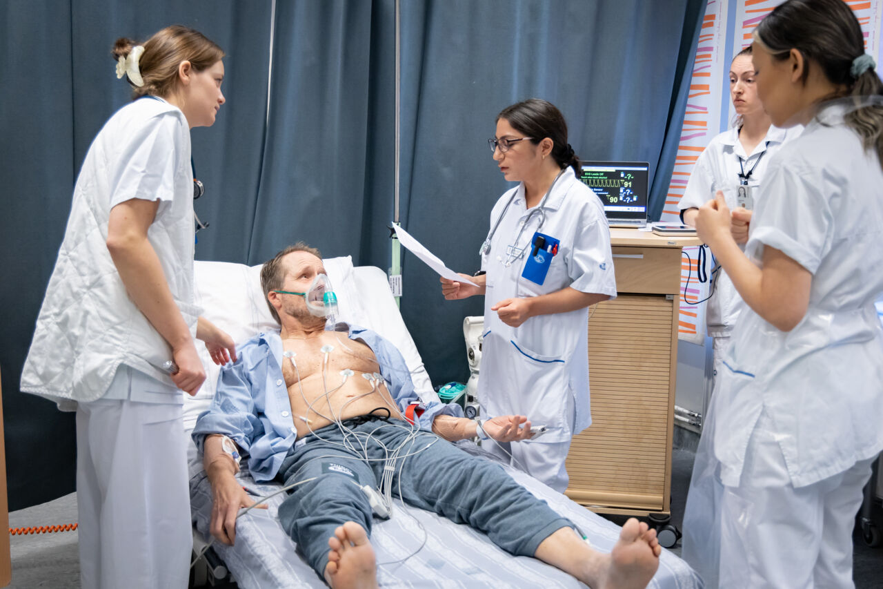Läkarstudenter undersöker en simulerad patient som ligger i en sjukhussäng.