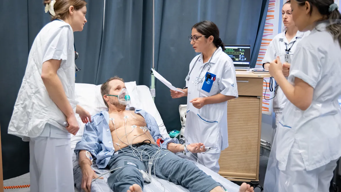 Läkarstudenter undersöker en simulerad patient som ligger i en sjukhussäng.