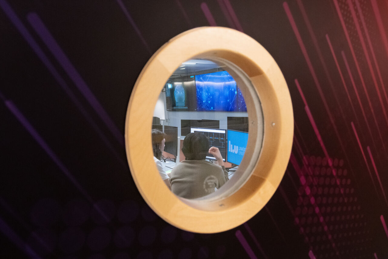 Photo of round window through which one sees students and computer screens.