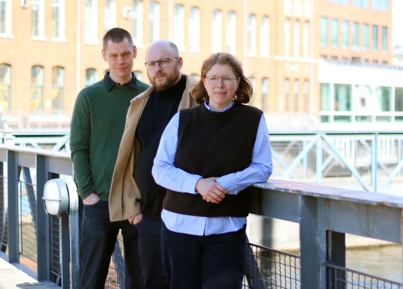 Tre personer står på en bro och lutar sig mot räcket