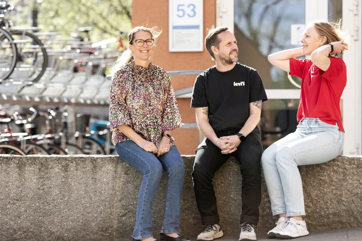 En bild på tre personer som sitter ute