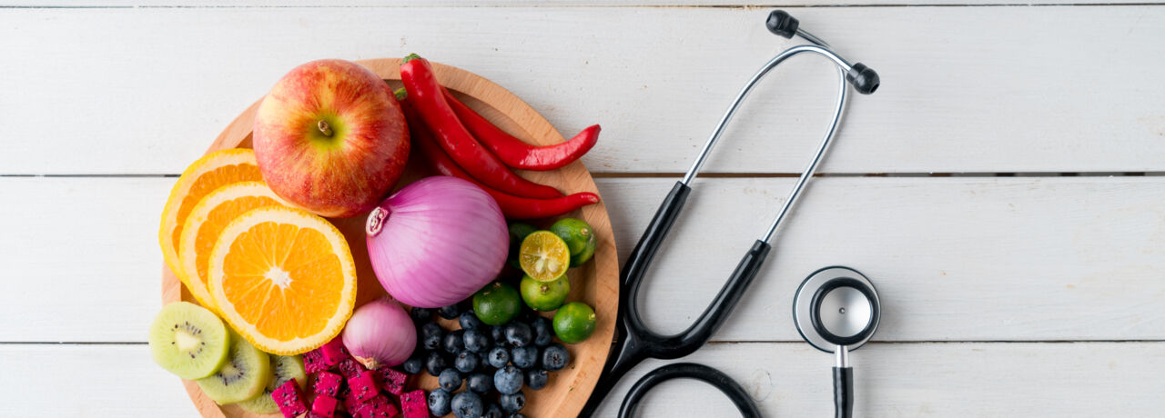 En bild visar stetoskop och en tallrik med frukt och grönsaker
