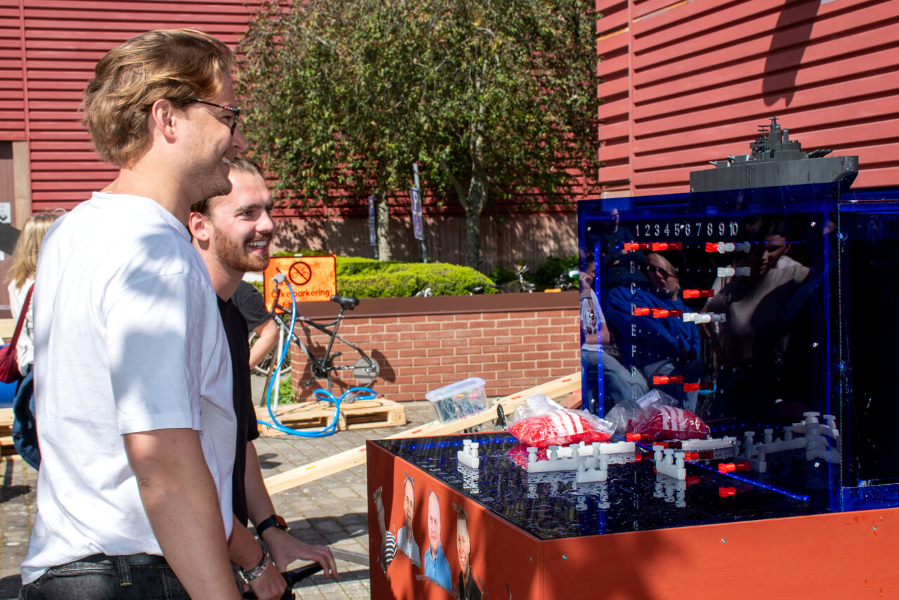 Två studenter står framför sänka skepp-spelet. 