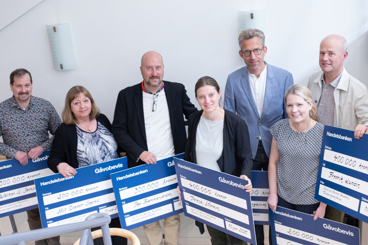 Sju män och kvinnor som håller i stora checkar