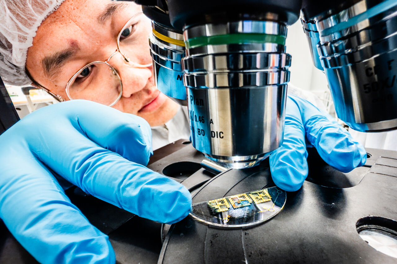 Forskare med blå plasthandskar vid mikroskop.