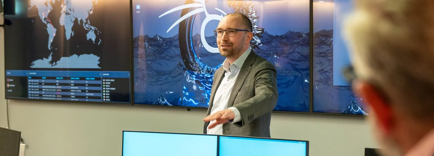 Mikael Asplund stands in front of big screens in the cybersecurity lab