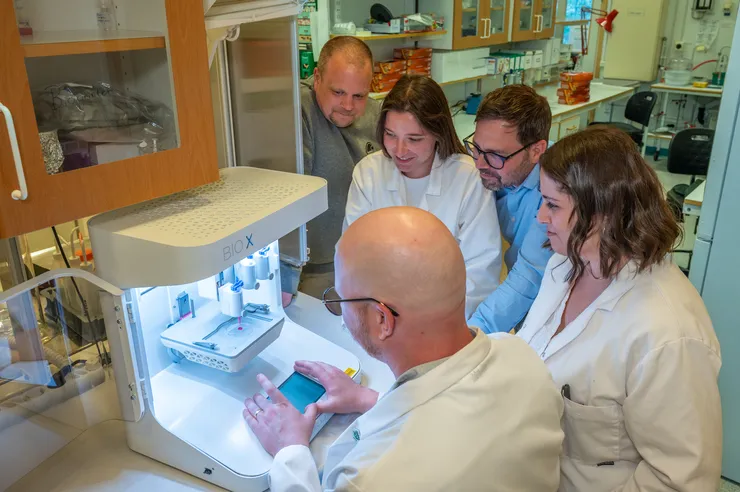 A group of researchers looking at a 3D printer.