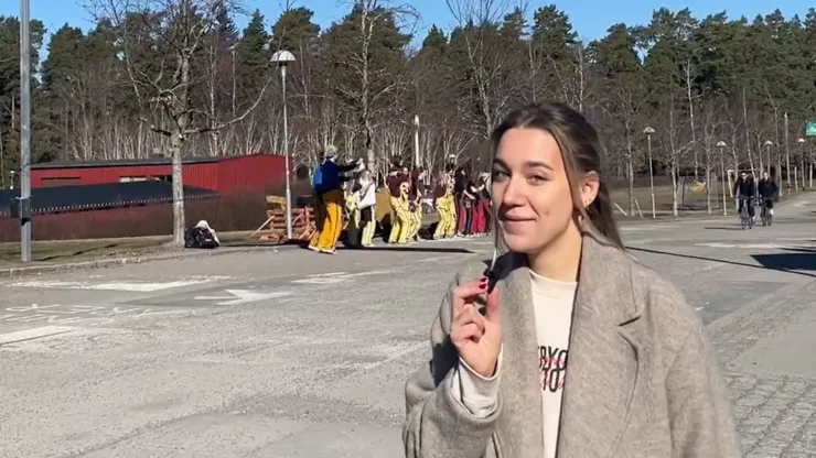 Tjej pratar in i kameran framför studenter i märkesbacken